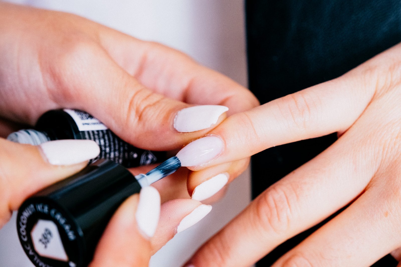Close up picture of beautician painting nails of a female client in a beauty center. White nails, coconut color. Concept: well being
