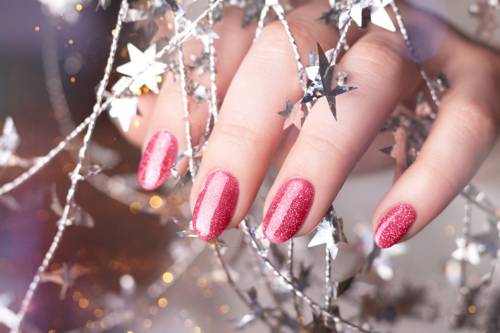 Female hand with beautiful holiday manicure - viva magenta, pink glitter nails with silver twisted wire with stars. Nail care concept